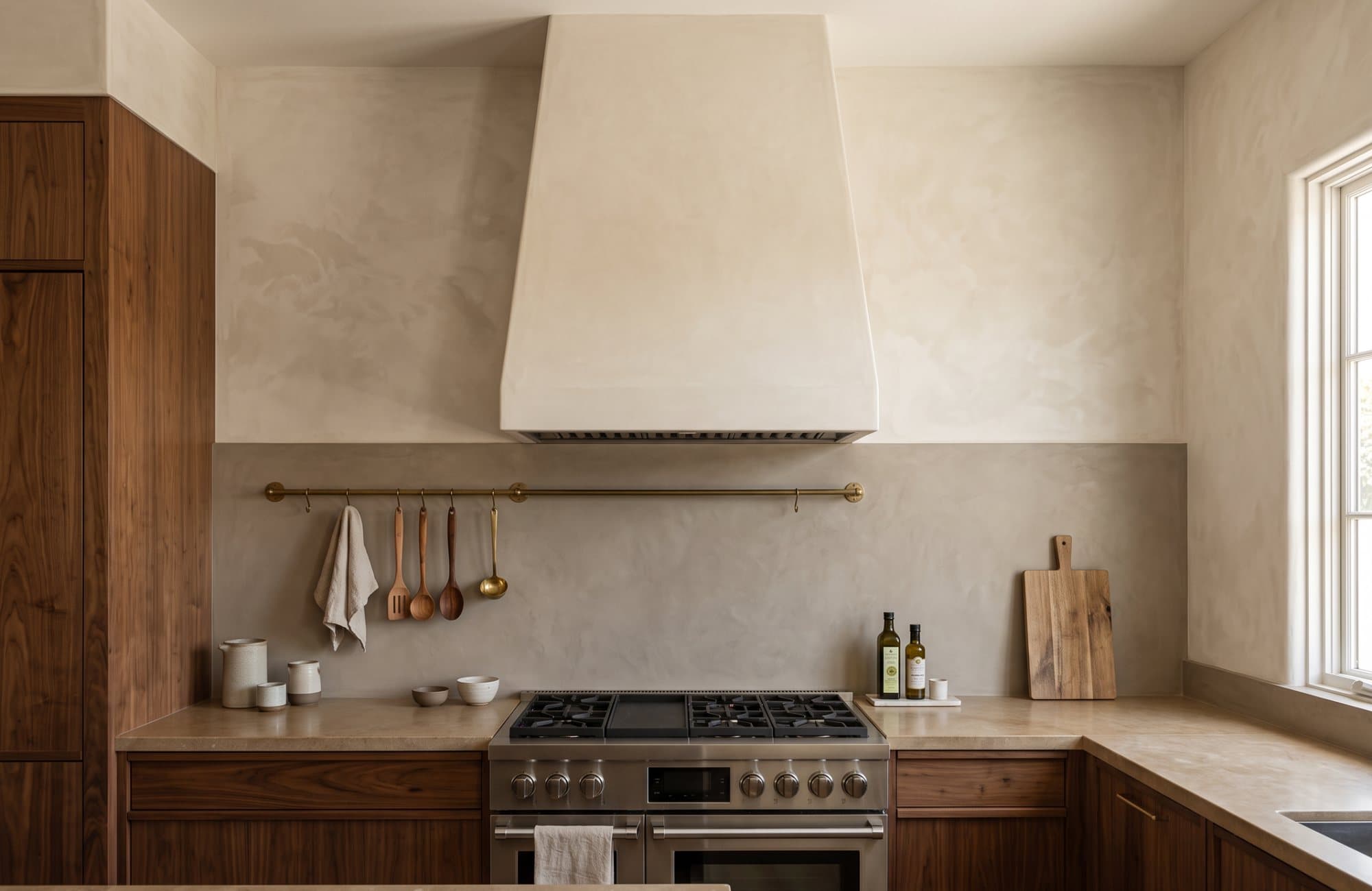 A kitchen centred on a tapered range hood in bone-white Venetian plaster over a professional range