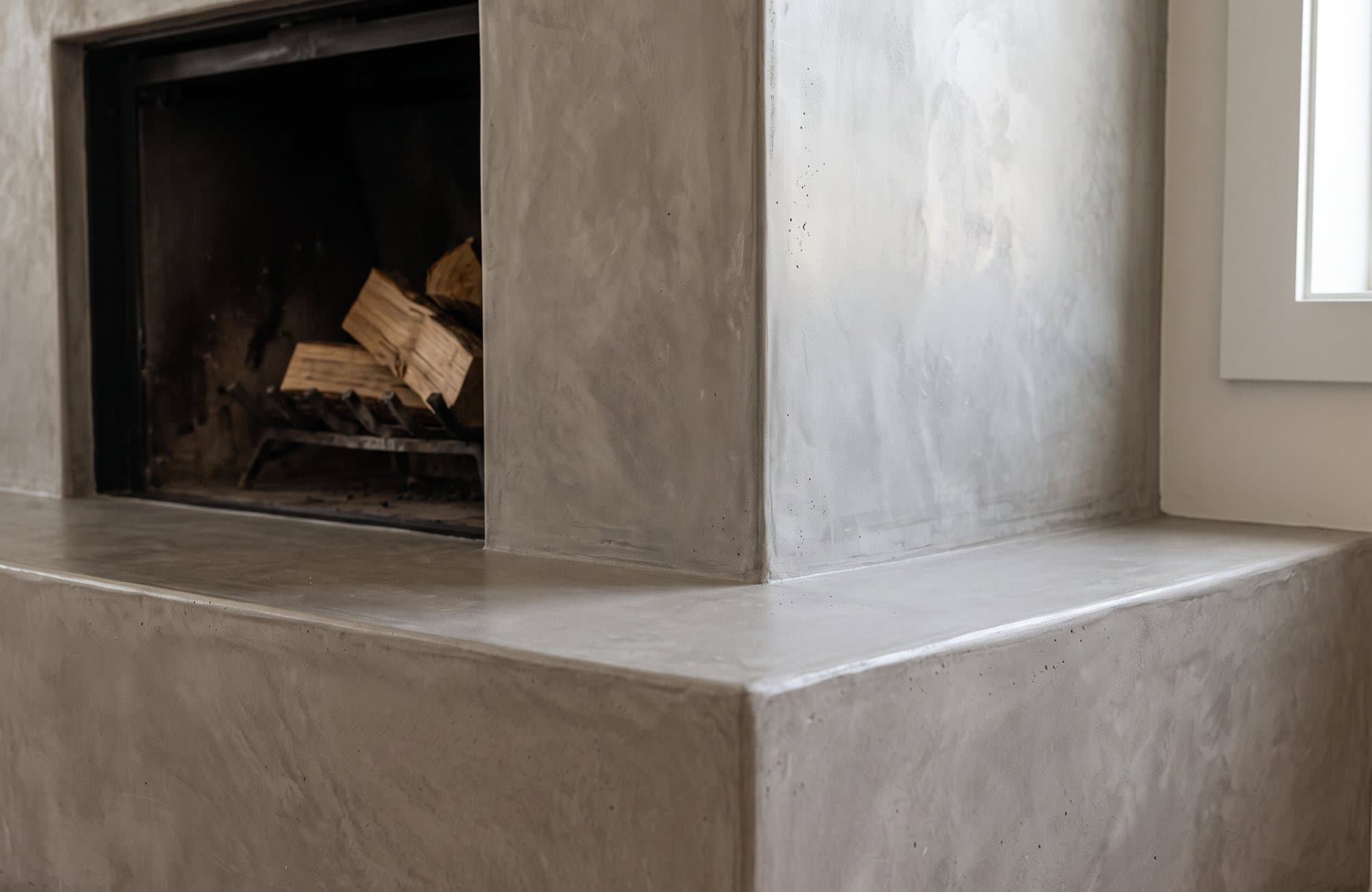 Close-up of the microcement hearth edge beside the uncoated black firebox