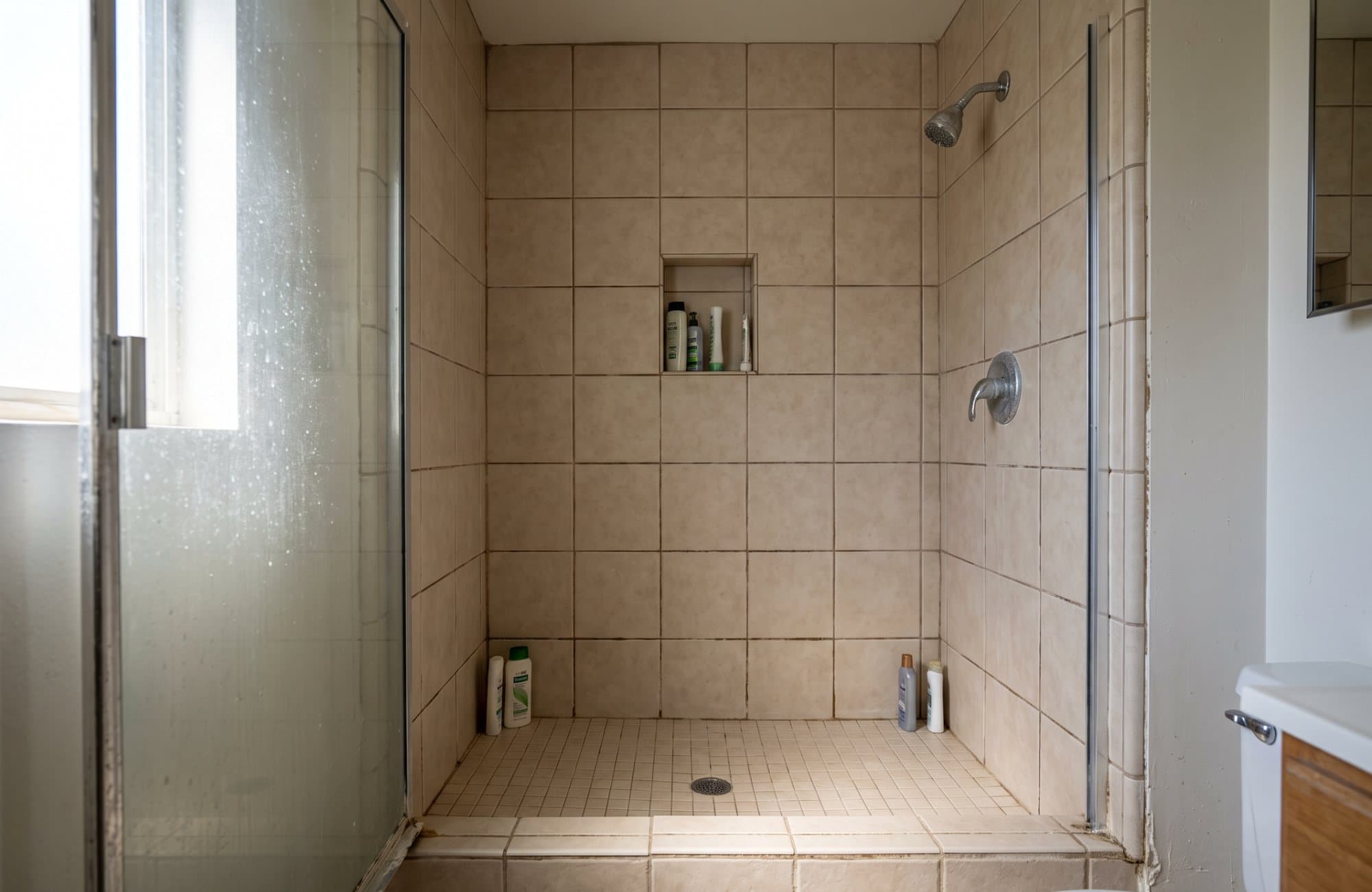 A typical starting point: a 1990s shower in beige tile with dark grout