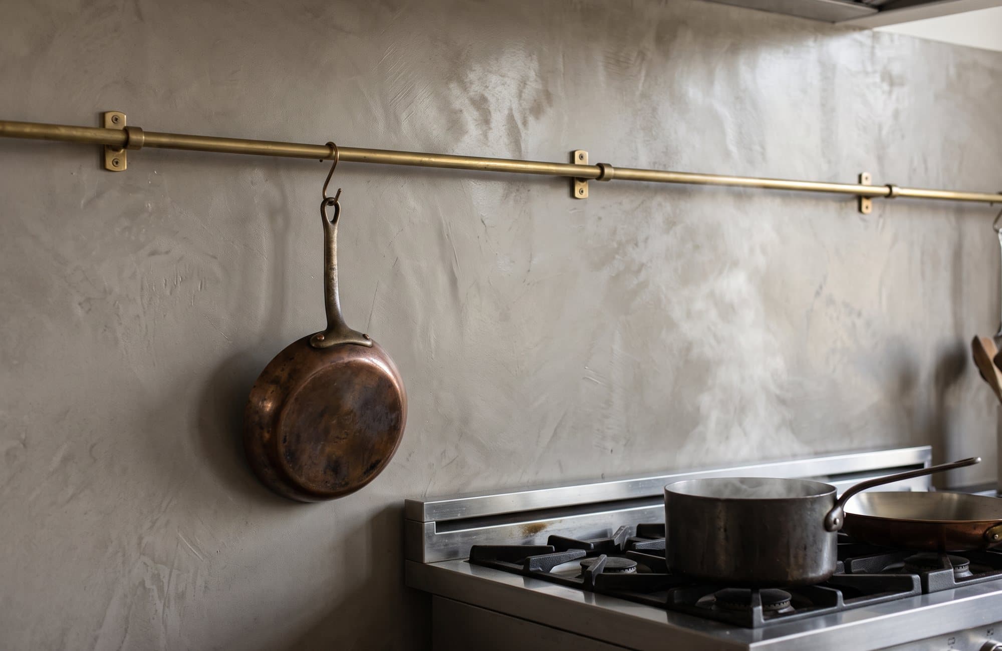A warm grey microcement backsplash behind the range with a copper pan
